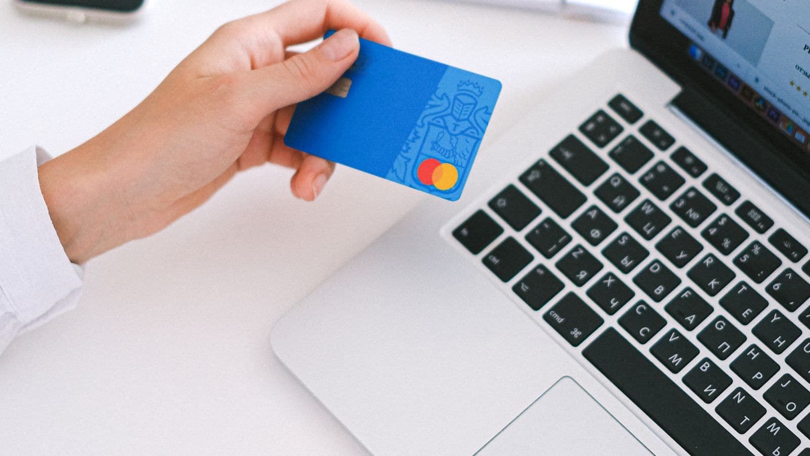 Hand holding a credit card over a laptop while reviewing a purchase